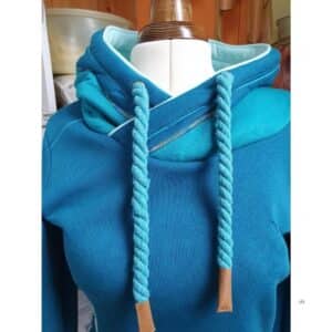 Blauer Hoodie auf einer Schneiderpuppe mit überkreuzter Kapuze, kontrastfarbigem Innenfutter, dekorativen Ziernähten und dicken Kordeln in Türkis.