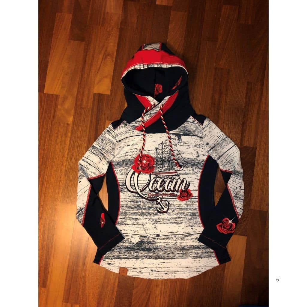 Hoodie mit maritimem Design in Dunkelblau, Weiß und Rot auf einem Holzboden. Der Hoodie besitzt eine überkreuzte Kapuze, dekorative Stickereien und Kordeln.