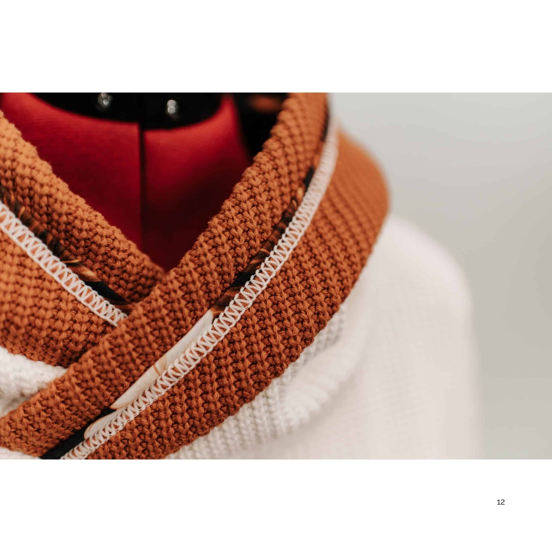 Nahaufnahme eines Hoodies mit breitem Schalkragen aus grob gestricktem Stoff in Rostbraun und kontrastierender heller Covernaht.