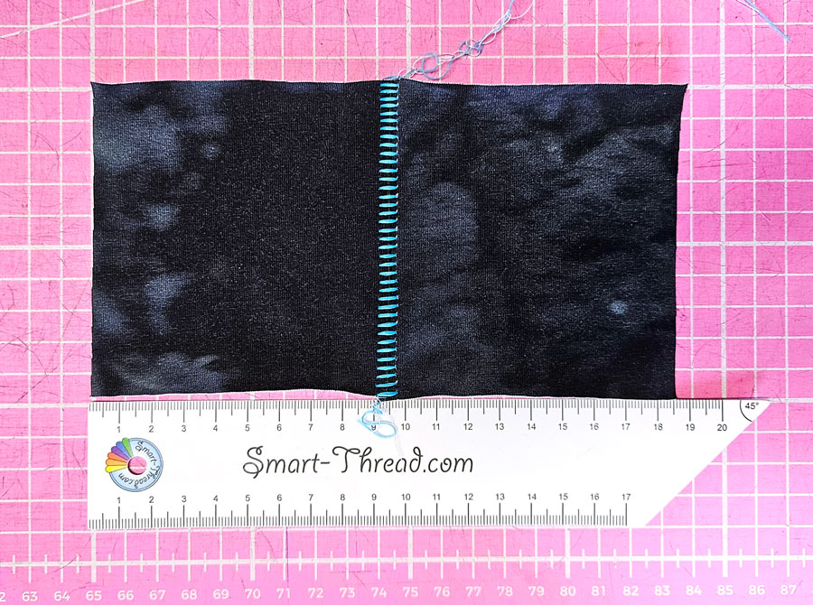 Auseinandergezogene Flachnaht Overlock mit dekorativer Leiteroptik auf dunklem Stoff.