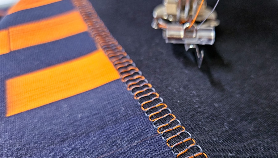 Detail einer dekorativen Covernaht mit orangefarbenem und dunklem Garn auf dem Sweatshirt-Sakko.