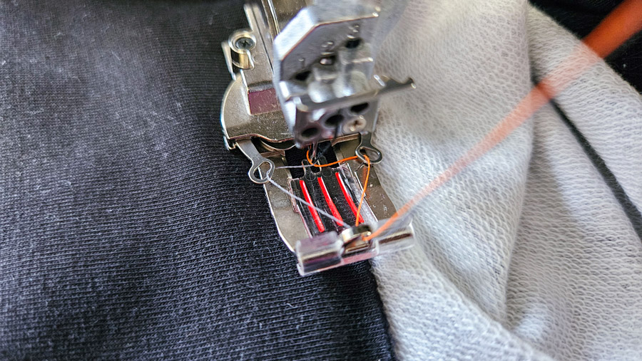 Covermaschine näht den Kragen eines Sweatshirt-Sakkos mit Kettstich und orangefarbenem Garn an.