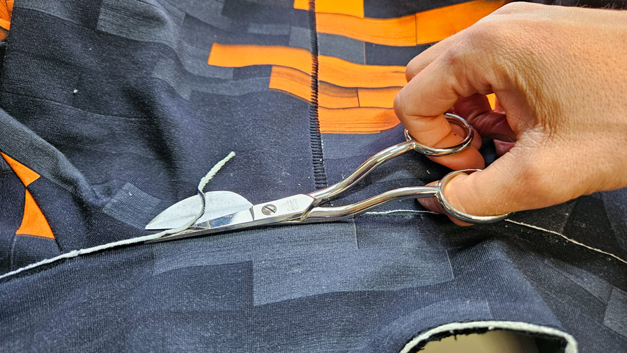 Offene Stoffkanten eines Sweatshirt-Sakkos werden mit einer Applikationsschere sauber zurückgeschnitten.