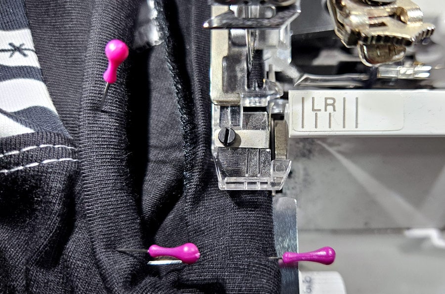 Eine Wave-Flachnaht wird mit der Overlock am Ärmelsaum eines Shirts genäht.