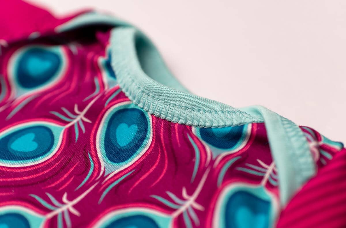 Nahaufnahme eines Halsausschnitts mit hellblauem Bündchen an einem pink gemusterten Babybody.