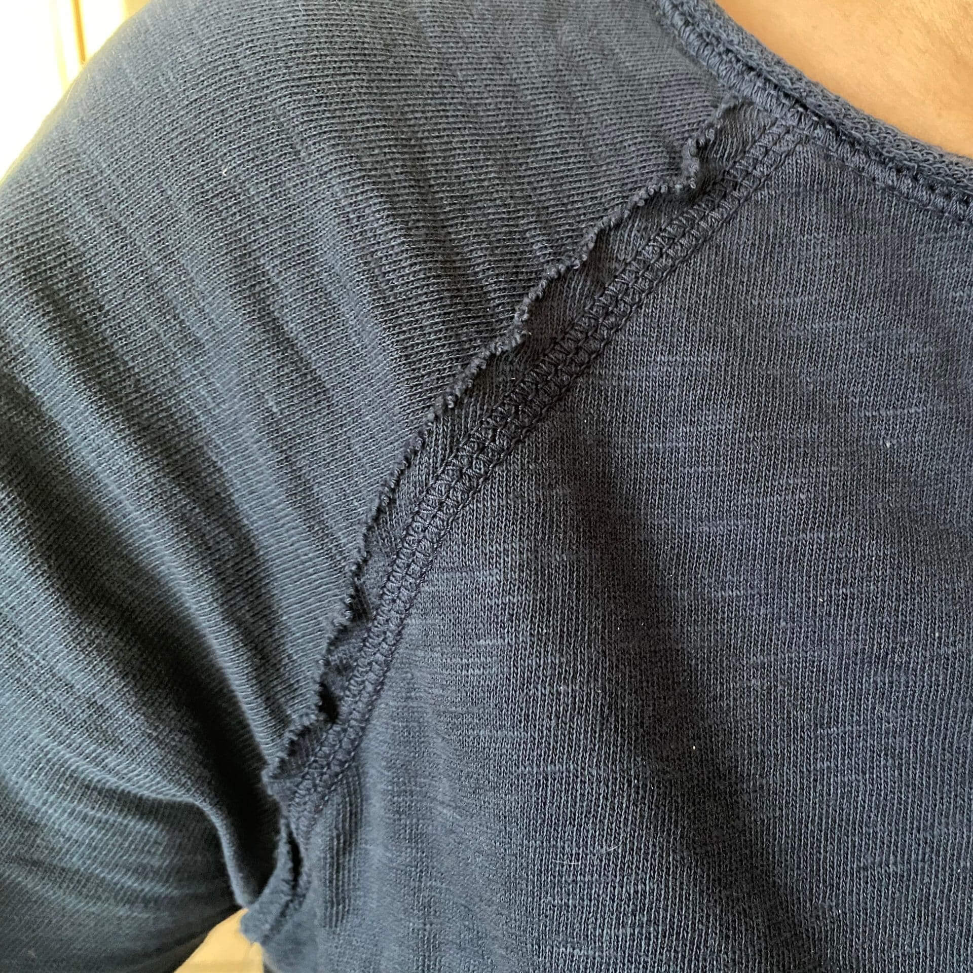 Nahaufnahme eines dunkelblauen Shirts mit dekorativer Overlocknaht entlang der Schulterpartie im Destroyed Look