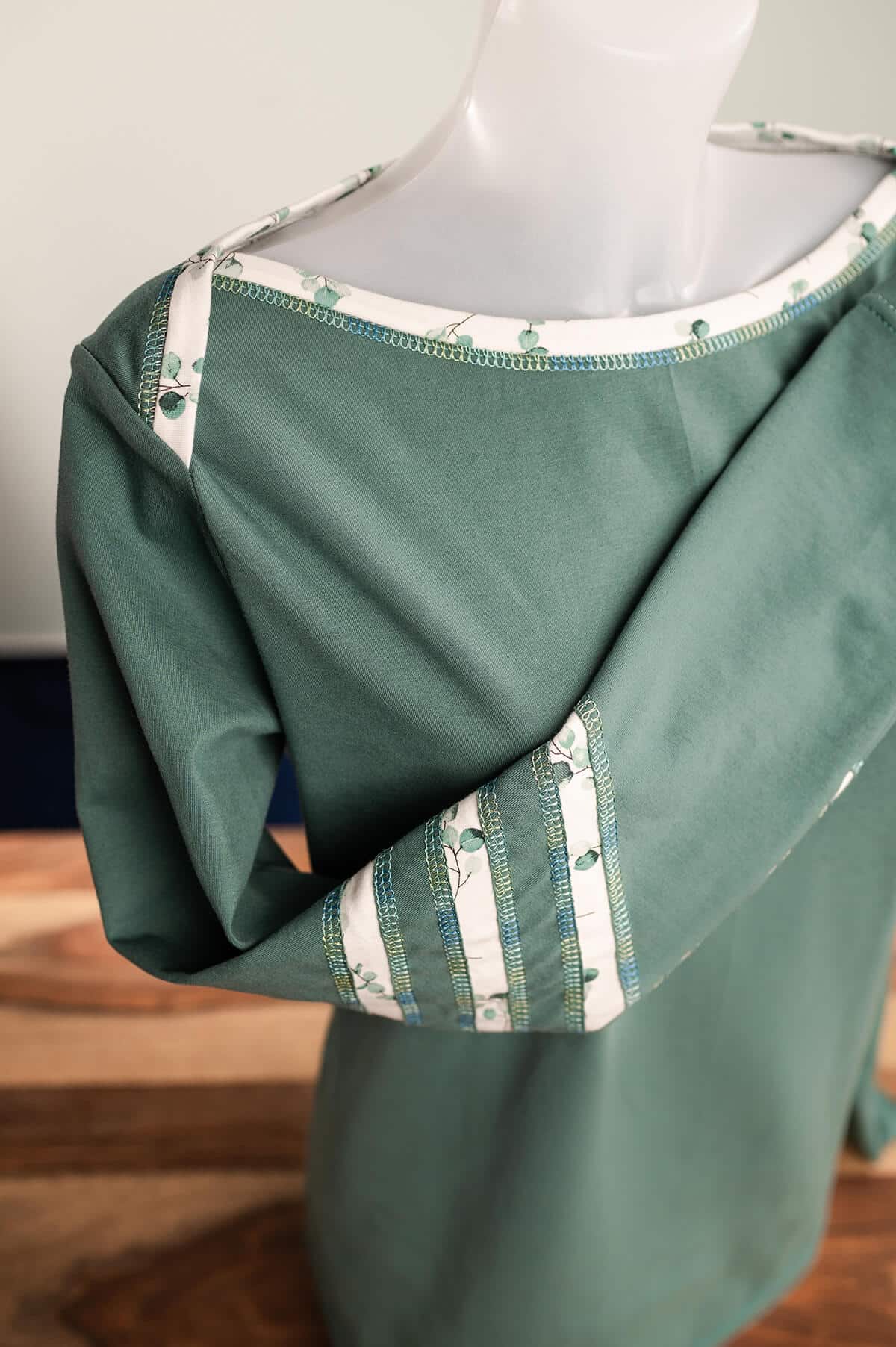 Grünes Langarmshirt mit dekorativen Covernähten und Applikationen am Ärmel und einem amerikanischen Ausschnitt.