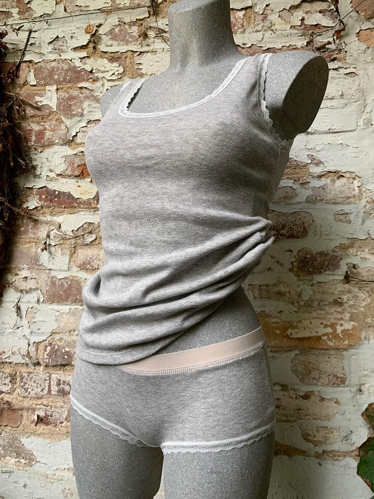 Hellgraues Unterhemd und passende Panty aus Jersey mit Spitzenabschlüssen auf einer Schneiderbüste.