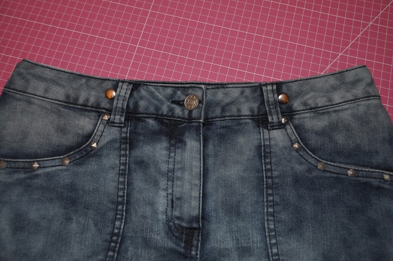 Vorderseite des Jeansrockbunds mit Knopf, Reißverschluss, Gürtelschlaufen und Eingrifftaschen.