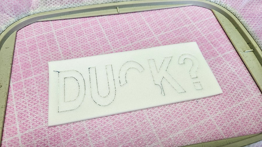 Perforierter Stickschaum mit dem Schriftzug „DUCK“ im Stickrahmen.