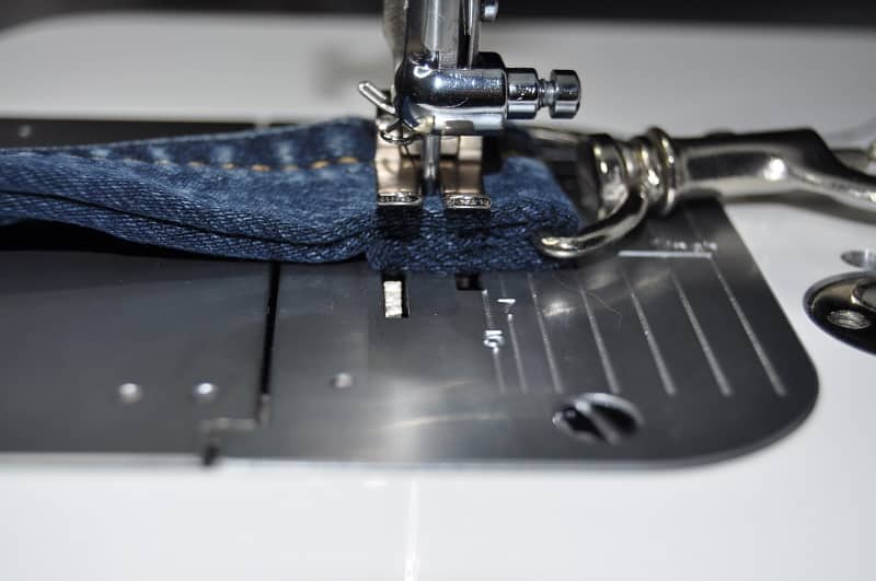 Ein Karabinerhaken wird an mehreren Lagen Jeansstoff des Taschenträgers mit der Nähmaschine befestigt.