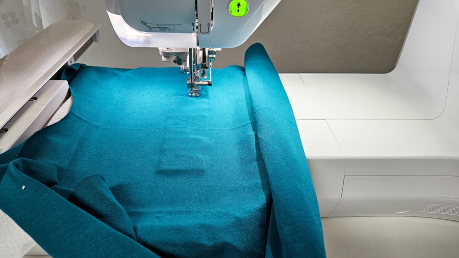 Türkisfarbenes Shirt-Vorderteil liegt in der Stickmaschine und wird für das Sticken eines Heftrahmens vorbereitet.