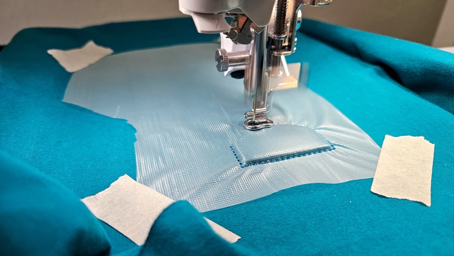 Avalon-Film liegt über dem türkisfarbenen Jersey und wird vor dem Sticken mit Kreppband fixiert.