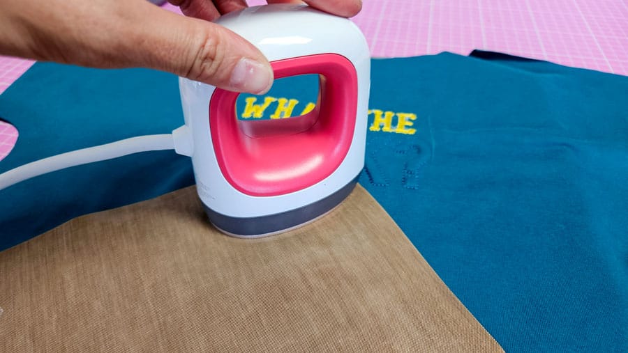 Gelbes Enten-Bügelbild wird mit einem Mini-Bügeleisen auf ein türkisfarbenes Shirt aufgebracht.