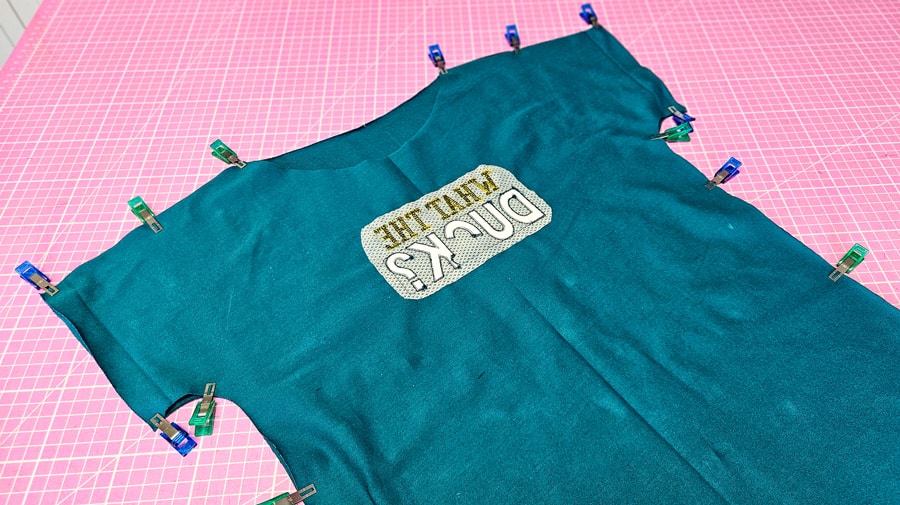 Vorder- und Rückenteil eines türkisfarbenen Shirts sind an Schulter- und Seitennähten mit Stoffklammern zusammengesteckt.