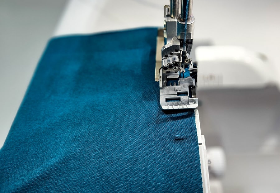 Türkisfarbener Jerseystoff wird mit der Overlockmaschine zusammengenäht und versäubert.