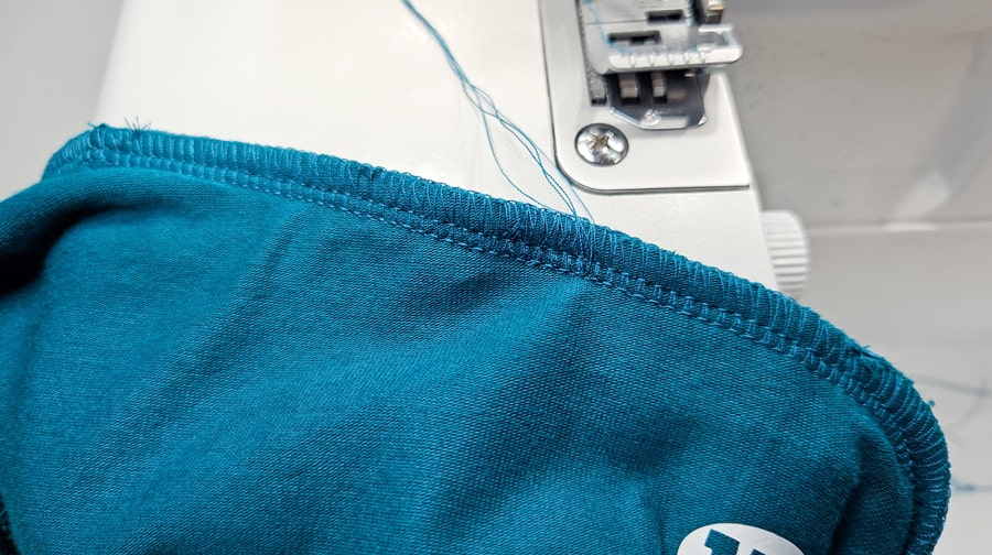 Saubere Overlocknaht am Halsausschnitt eines türkisfarbenen Shirts mit Fadenenden.