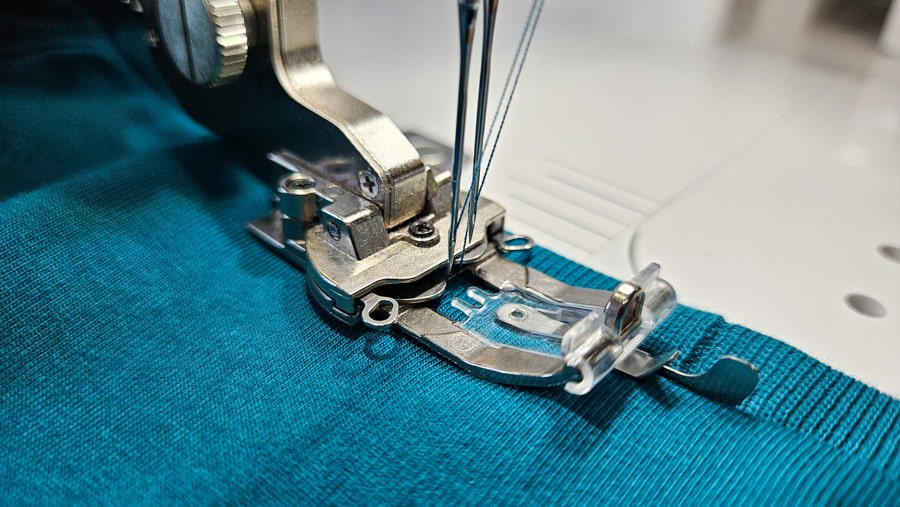 Halsbündchen eines türkisfarbenen Shirts wird mit einer Coverstitch-Maschine abgesteppt.